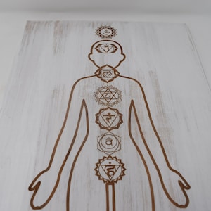May include: A white wooden board with a brown outline of a human figure and seven chakras, each with a different symbol and color.