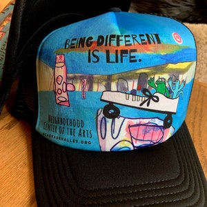 May include: Black trucker hat with a colorful design featuring a cartoon car, a frog, and the text "Being Different is Life." The hat also has the text "Neighborhood Center of the Arts" and a website address.