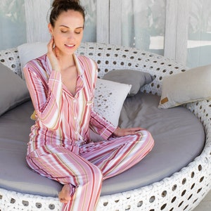 May include: A woman wearing a pink and white striped pajama set sits on a white wicker circular bench. The bench has a gray cushion and is surrounded by white walls.