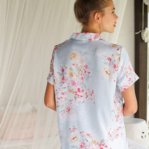 Puede incluir: Una camiseta de pijama azul claro con estampado floral. La camiseta tiene mangas cortas y cuello.