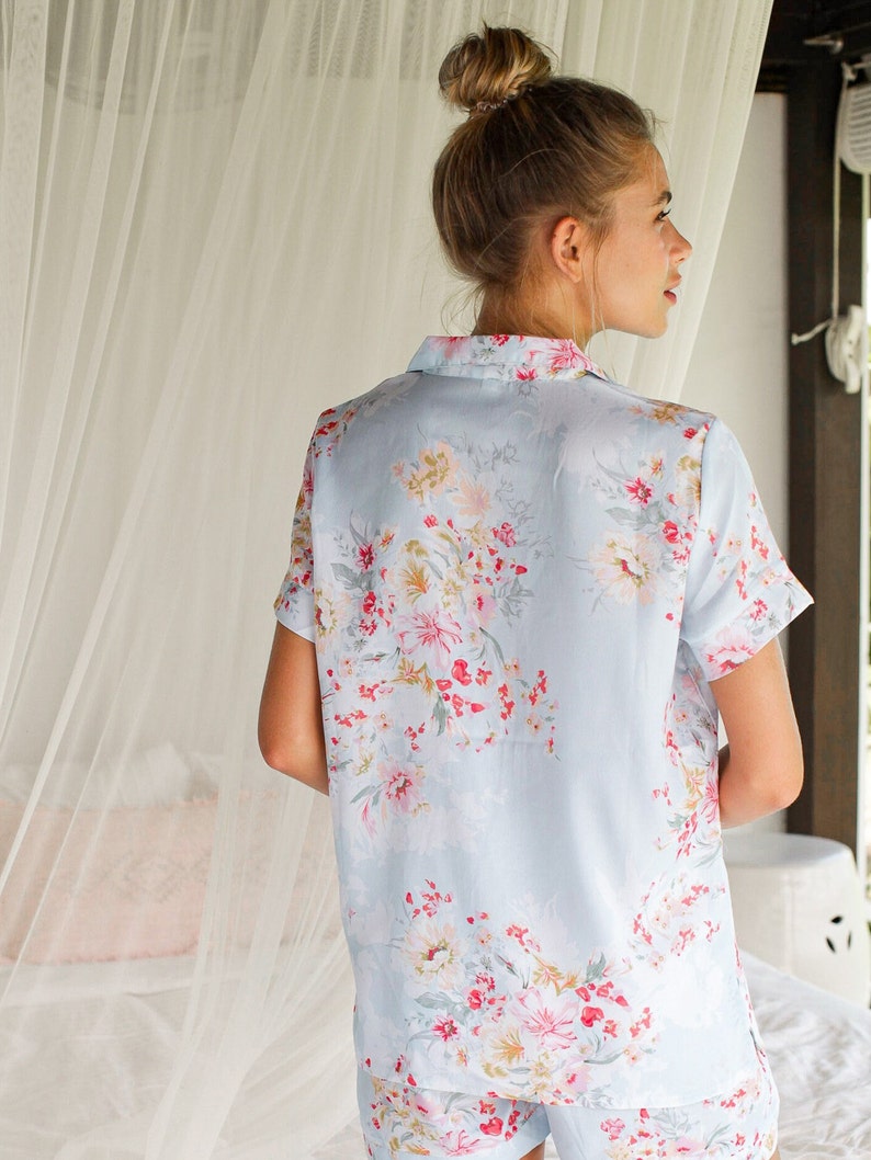Puede incluir: Una camiseta de pijama azul claro con estampado floral. La camiseta tiene mangas cortas y cuello.