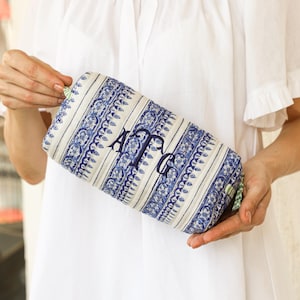 May include: A rectangular, quilted cosmetic bag with a blue and white floral pattern. The bag features a monogram in navy blue thread. The bag is held against a white background.