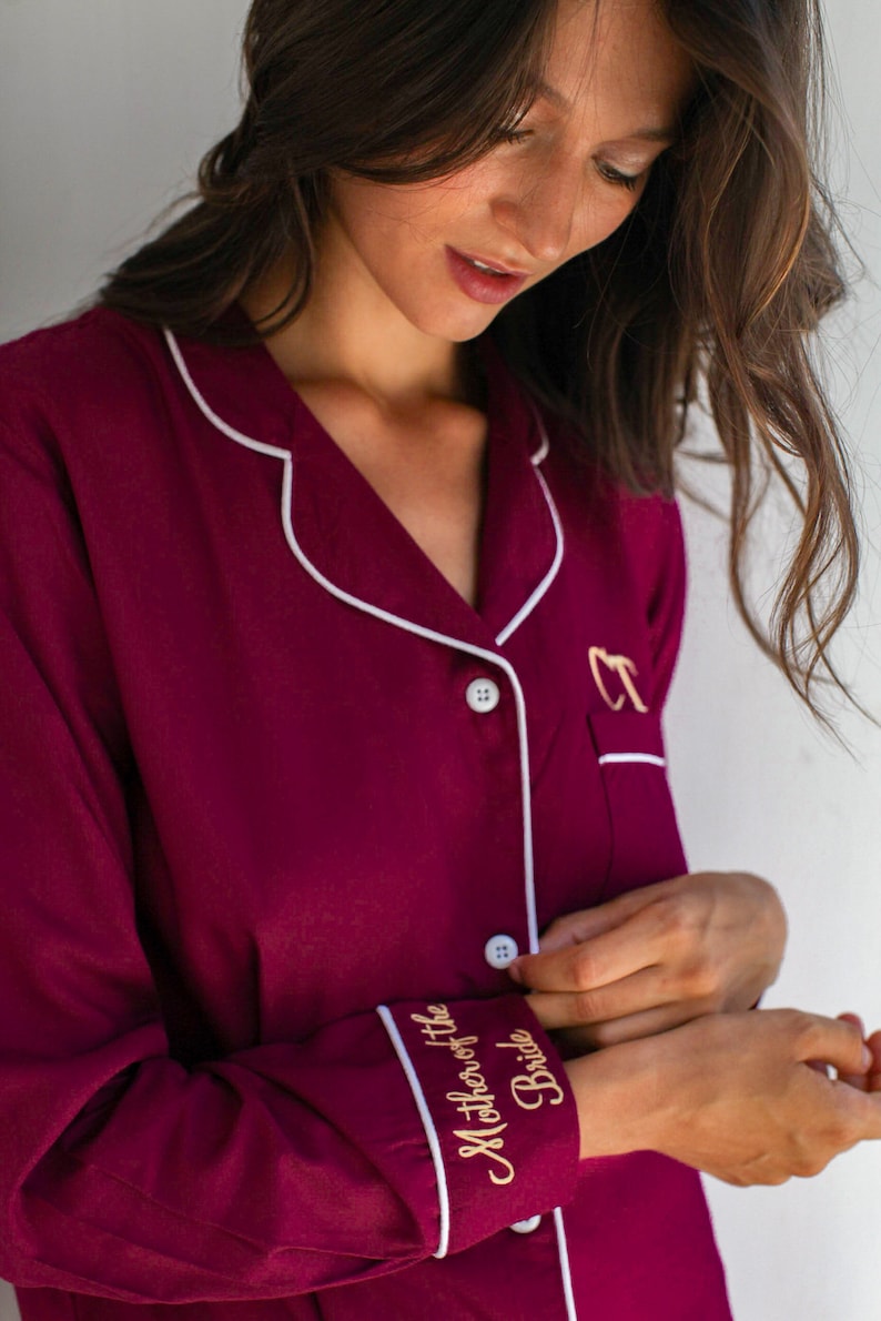 May include: Burgundy pajama top with white piping and gold embroidery that reads "Mother of the Bride".
