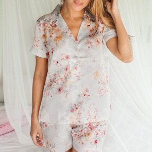 May include: A gray and white floral print pajama set with short sleeves and shorts. The top has a collared neckline and button closure.