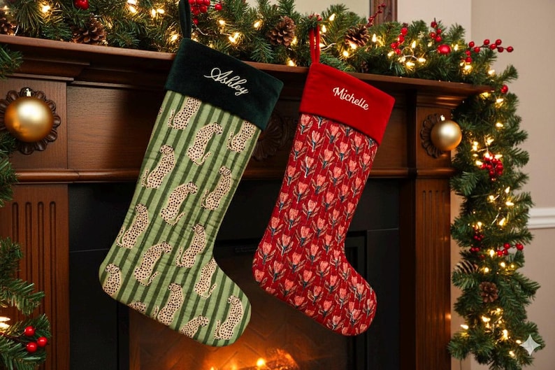 May include: Two Christmas stockings hang above a fireplace. One is green with a leopard print and the name "Ashley" embroidered on the cuff. The other is red with a floral pattern and the name "Michelle". Festive garland and lights decorate the mantel.
