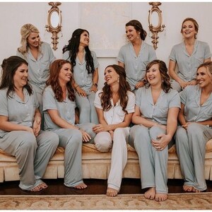 May include: A group of eight people wearing matching light blue pyjamas are sitting on a cream-coloured sofa. They are all smiling and looking at the camera.