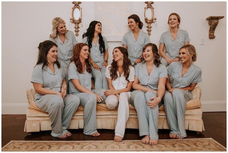 May include: A group of eight people wearing matching light blue pyjamas are sitting on a cream-coloured sofa. They are all smiling and looking at the camera.