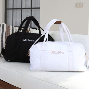May include: Two personalized travel bags, one black with the text "Mr. Sweis" and one white with the text "Mrs. Sweis" in pink.