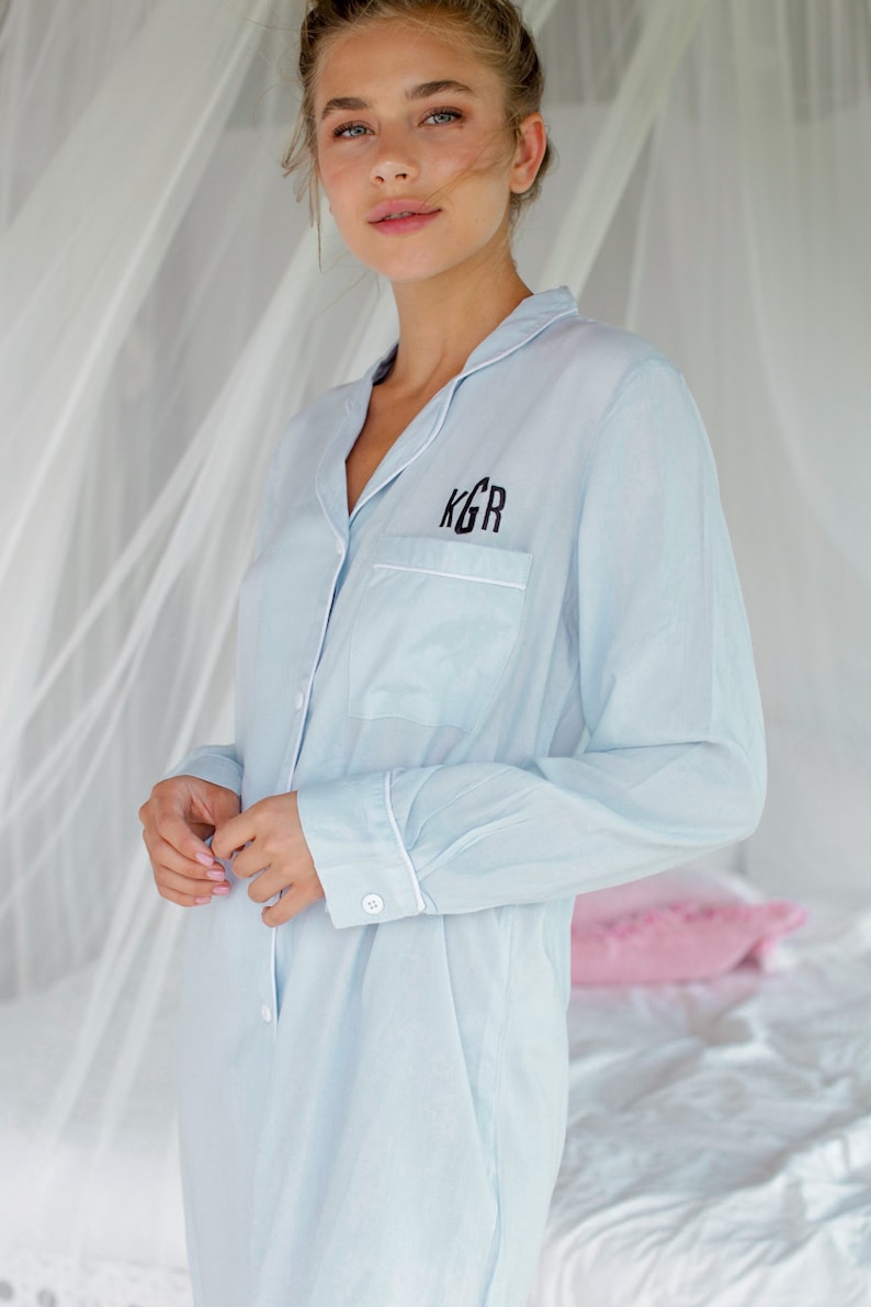 May include: A light blue button-down shirt with white piping and a black embroidered monogram "KGR" on the chest pocket.