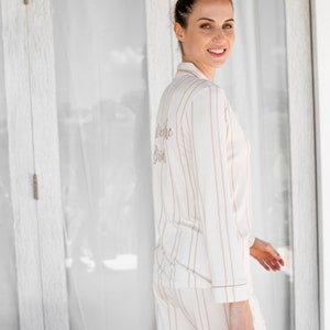 Puede incluir: Una mujer con un pijama a rayas blancas y marrones con el texto "Future Bride" bordado en la espalda.