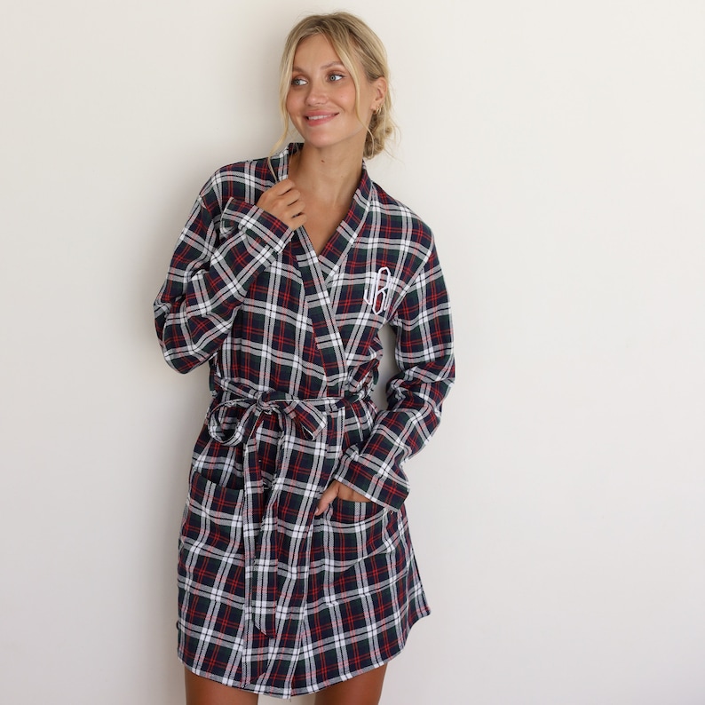 May include: A red, green, and white plaid robe with a white monogram on the left chest. The robe has a shawl collar, long sleeves, and a tie belt.