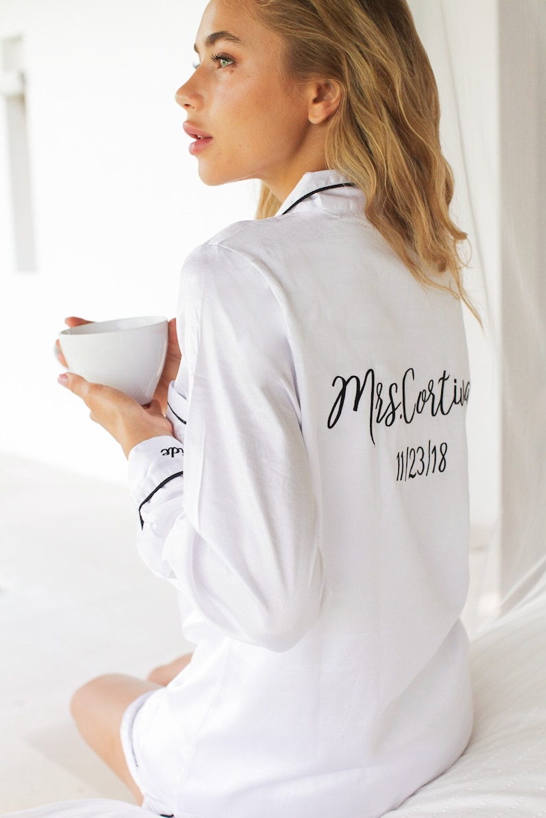 May include: White satin pajama top with black piping and the text "Mrs. Cortina 11/23/18" embroidered on the back.