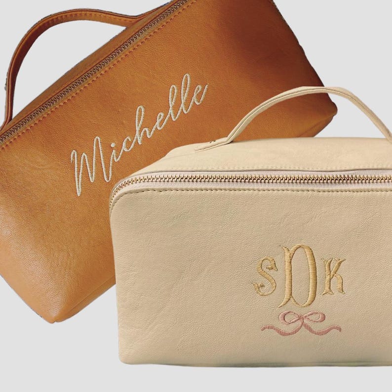 May include: Two zippered cosmetic bags, one brown with the name "Michelle" embroidered in white, and the other beige with the monogram "S.D.K." embroidered in gold with a pink ribbon.