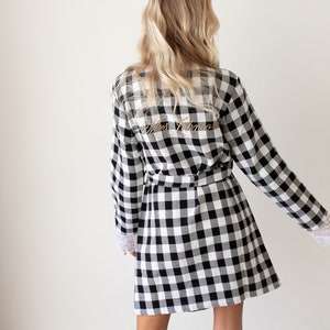 May include: Black and white checkered robe with long sleeves and a sash. The back of the robe has the text "Mrs. Johnson" embroidered in gold.