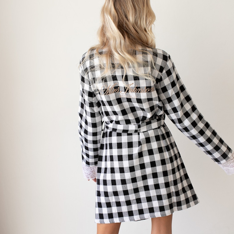 May include: Black and white checkered robe with long sleeves and a sash. The back of the robe has the text "Mrs. Johnson" embroidered in gold.