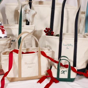 Puede incluir: Una colección de bolsas de lona de varios tamaños y colores. Algunas bolsas tienen iniciales o nombres personalizados bordados. Cintas rojas y adornos decorativos añaden un toque festivo. Las bolsas tienen correas y ribetes de diferentes colores.