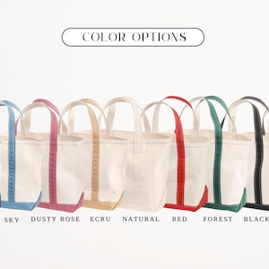 May include: A selection of canvas tote bags in colours such as navy, sky blue, dusty rose, ecru, natural, red, forest green, black, and olive. Each bag has contrasting trim and handles. The text "COLOR OPTIONS" is displayed above.