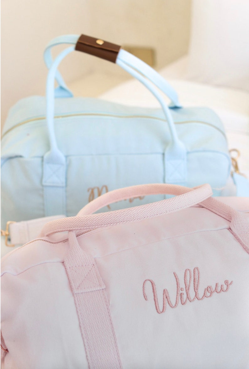 May include: Two canvas duffel bags, one light blue and one pink. The pink bag has the name "Willow" embroidered on it in a cursive font.