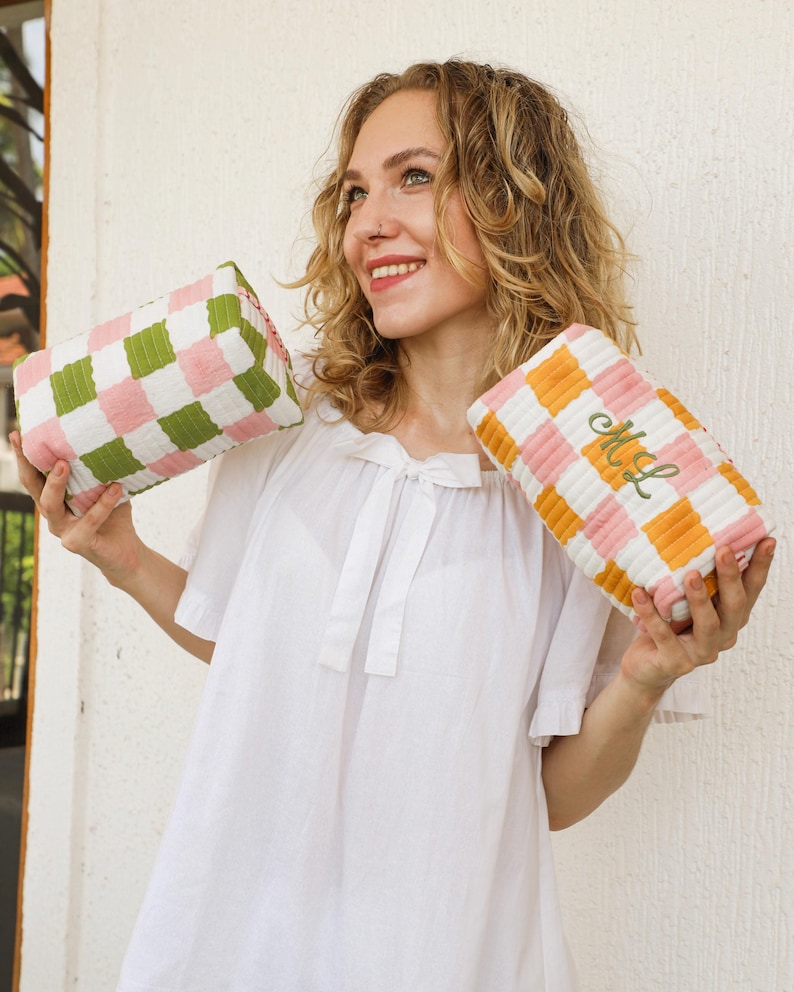 May include: Two rectangular cosmetic bags with a checkered pattern. One bag features green, pink, and white squares, while the other has orange, pink, and white squares. The second bag has the embroidered initials "ML" in green.