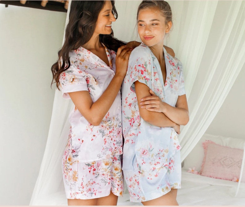 May include: Two people wearing floral print pajamas. The person on the left is wearing a pink and white floral print pajama set. The person on the right is wearing a light blue and white floral print pajama set.