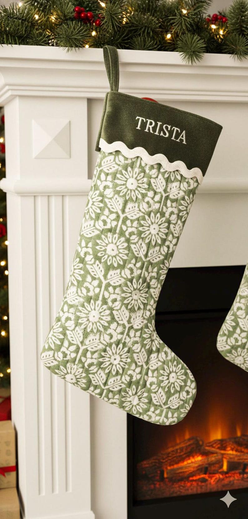 May include: A green and white Christmas stocking with a floral pattern. The stocking has a green cuff with the name "TRISTA" embroidered in white. The stocking is hanging on a white mantel.