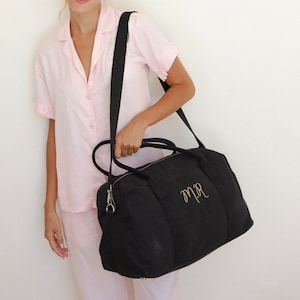 May include: A black canvas travel bag with a gold embroidered monogram "M.R."  The bag has a top zipper closure and a long adjustable shoulder strap.