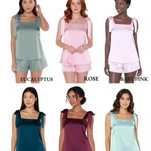 Peut inclure: Ensemble de pyjamas cami &agrave; n&oelig;uds en satin, disponibles en eucalyptus, rose, rose b&eacute;b&eacute;, sarcelle, bordeaux et aqua. Chaque ensemble comprend un haut cami &agrave; col carr&eacute; avec des bretelles nou&eacute;es et un short assorti. Le texte "COLORS" et "TIE KNOT CAMI PJ SET" est en haut.
