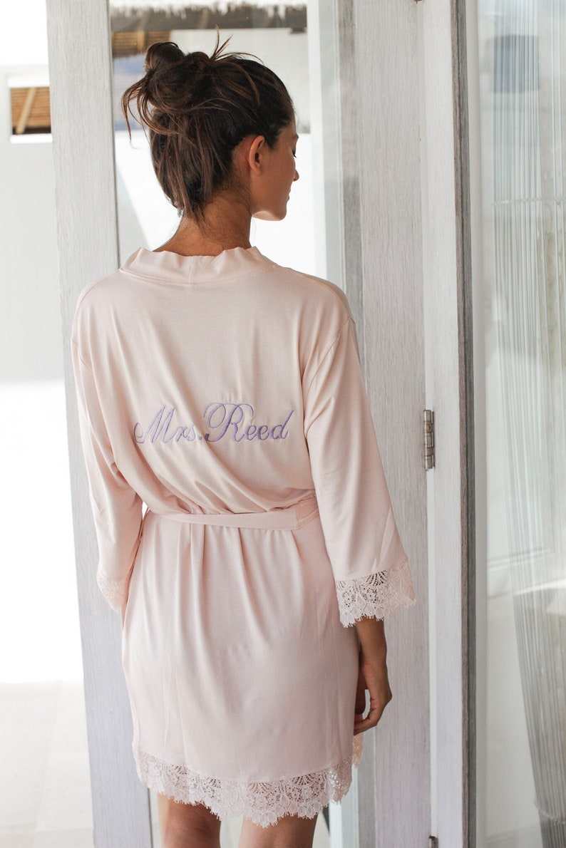 May include: A pale pink satin robe with lace trim and the text "Mrs. Reed" embroidered on the back.