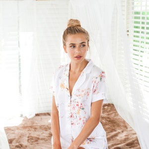 Puede incluir: Una mujer con un top de pijama blanco de botones con estampado floral. El top tiene mangas cortas y cuello. La mujer lleva el pelo recogido en un mo&ntilde;o.
