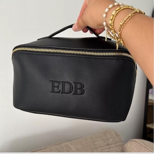 May include: Black leather zippered travel makeup bag with a gold zipper and the initials "EDB" embossed on the front.