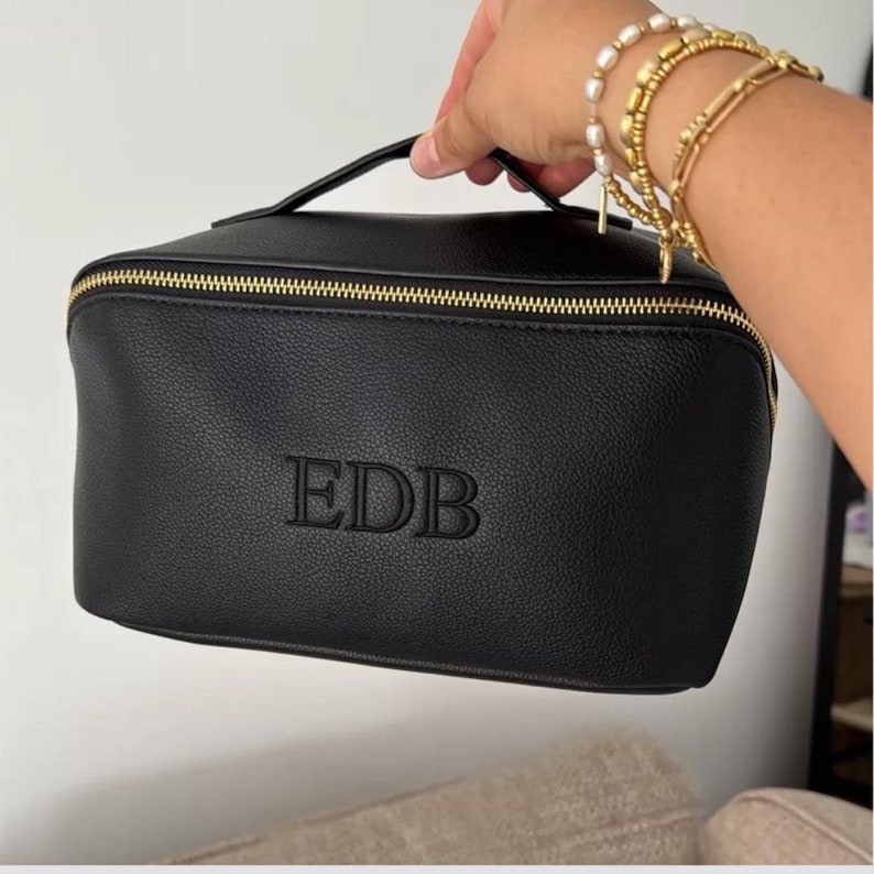 May include: Black leather zippered travel makeup bag with a gold zipper and the initials "EDB" embossed on the front.