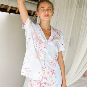 May include: A light blue pajama set with a floral print. The top has short sleeves and a button-up front. The shorts have a relaxed fit.