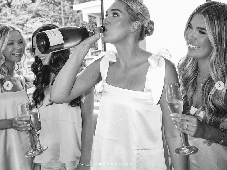 Peut inclure: Image en noir et blanc d'un groupe de femmes en f&ecirc;te. Une femme boit &agrave; une bouteille de champagne, tandis que d'autres tiennent des fl&ucirc;tes &agrave; champagne. Elles portent toutes des robes blanches. L'image est prise en ext&eacute;rieur.