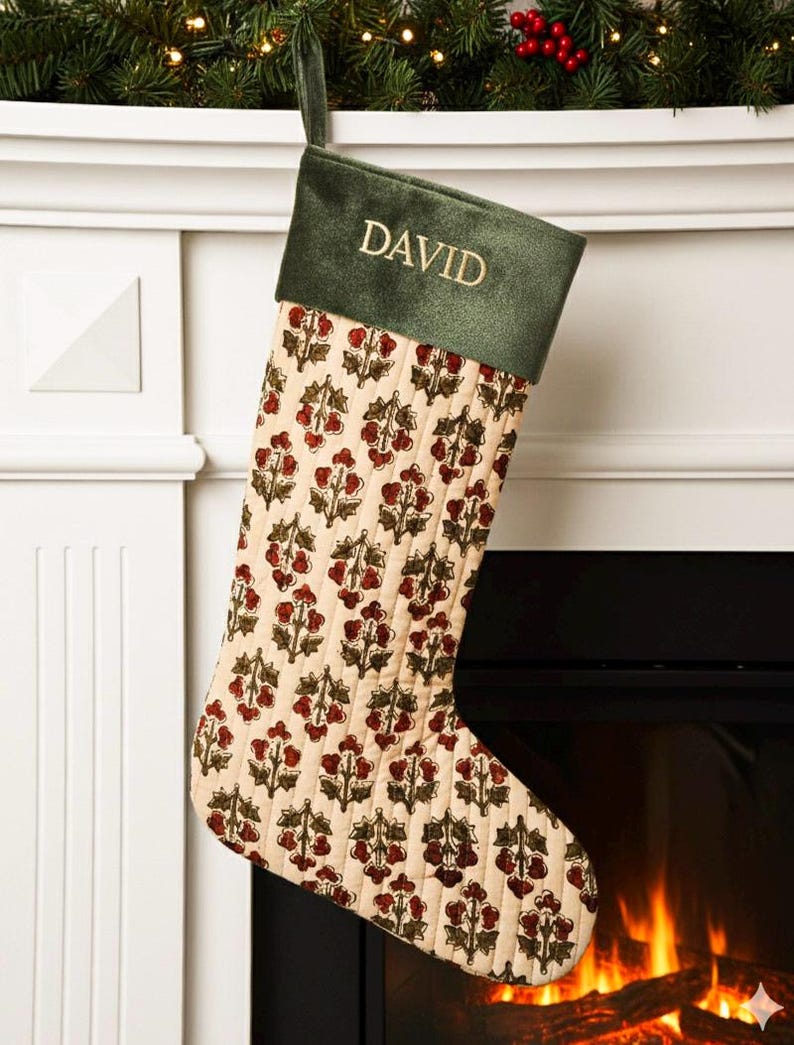 May include: A Christmas stocking with a green velvet cuff embroidered with the name "DAVID" in gold. The body of the stocking is cream-colored with a repeating pattern of red and green floral designs. A green loop is attached for hanging.