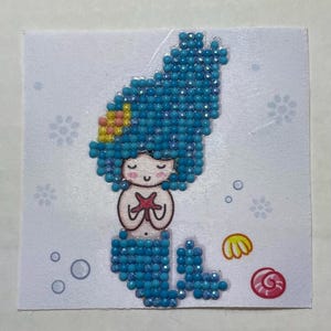 May include: A blue mermaid with yellow and pink hair holding a red starfish. The mermaid is surrounded by white flowers and blue bubbles.