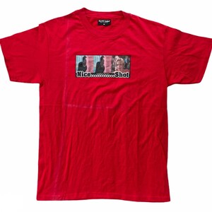 May include: Red t-shirt with a graphic print of a scene from the movie 'Dodgeball: A True Underdog Story'. The graphic features a group of people and the text 'Nice......Shot'.