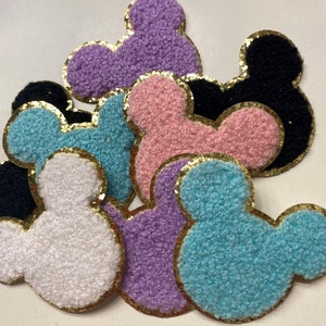 May include: A set of eight felt Mickey Mouse ears in various colors, including pink, purple, blue, white, and black. Each ear is trimmed with gold glitter.