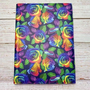 Può includere: Una copertina per quaderno in pelle blu scuro con un motivo di rose arcobaleno. Le rose sono colorate e vibranti, su uno sfondo blu scuro.