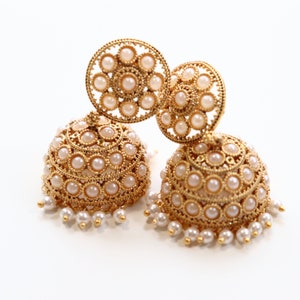 Peut inclure: Une paire de boucles d'oreilles en or avec des accents de perles. Les boucles d'oreilles sont rondes et ont un design délicat. Les perles sont blanches et disposées en cercle.