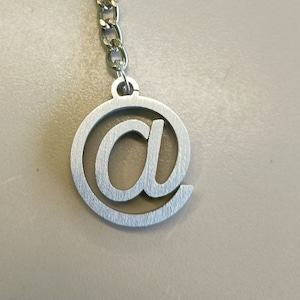 Può includere: Portachiavi in ​​argento con un ciondolo circolare con un simbolo chiocciola.