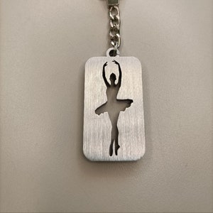Peut inclure: Porte-clés argenté avec un charme en silhouette de ballerine. Le charme est découpé dans le métal et a une finition brossée.