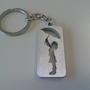 Puede incluir: Llavero de plata con un diseño recortado de una persona sosteniendo un paraguas.