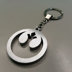 May include: A silver metal keychain featuring the Rebel Alliance symbol from Star Wars. The symbol is a circle with a line through it and two wings on either side.