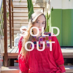 May include: A woman wearing a red embroidered blouse with colorful floral patterns and blue jeans. The text "SOLD OUT" is superimposed on the image.