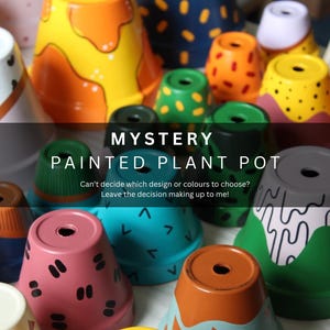 Puede incluir: Una colección de macetas pintadas con diversos diseños y colores. Los diseños incluyen puntos, triángulos y formas abstractas. El texto en la imagen dice "MYSTERY PAINTED PLANT POT".