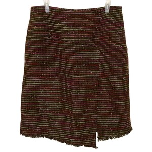 May include: A knee-length skirt crafted from a dark brown tweed fabric featuring horizontal stripes in vibrant pink, yellow, and white. The garment includes a subtle wrap-style front panel with a vertical slit and a frayed, raw-edge hemline.
