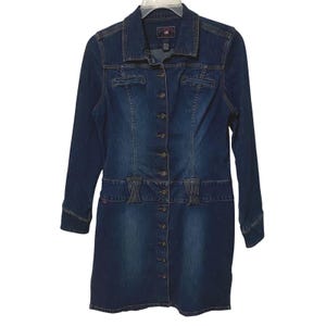 May include: A dark blue denim dress featuring a full-length button-down front, a classic collar, and long sleeves. The garment includes a horizontal waistband detail with two vertical stitched accents and a faded wash finish throughout the fabric.