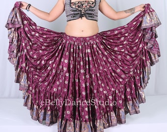 May include: A flowing, tiered skirt in shades of deep purple with a repeating pattern of gold accents. The skirt has a wide, ruffled hem with gold and blue patterned trim. The outfit includes a silver vest with black accents and a patterned top.