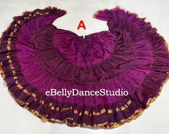 May include: A full, flowing belly dance skirt in shades of purple and burgundy, with gold trim along the ruffled edges. The skirt is circular, with a wide waistband and a layered design. The text "eBellyDanceStudio" is visible.