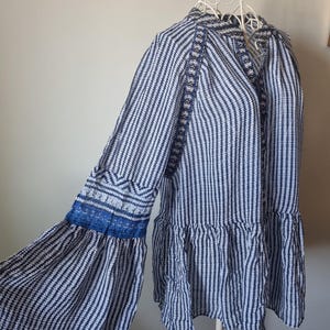 May include: A long-sleeved blouse with a vertical striped pattern in navy blue and white. The sleeves have a flared design with blue lace trim. The blouse is displayed on a white mannequin.